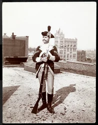 En man på ett hustak klädd i traditionell militäruniform med ett gevär i handen, 1895 (silvergelatintryck)